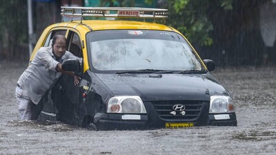 A taxi driver pushes his car as he tries to wade through a waterlogged street at Hindmata in Mumbai